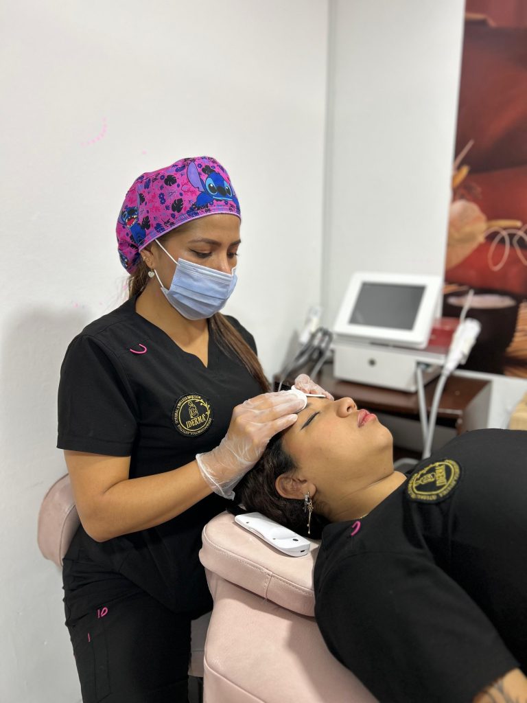 Profesional de estética realiza tratamiento facial avanzado a paciente en camilla rosa, con enfoque nítido en el equipo y el procedimiento.